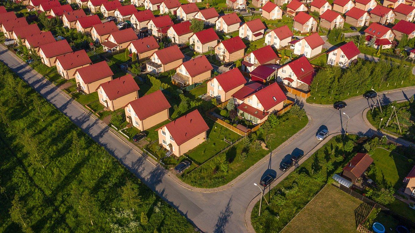 Cottage village view from the drone. suburbia on a summer day. Empty road next to cottage village. Similar houses with lawns. Cottage village with two-storey houses. Concept - buying a country house