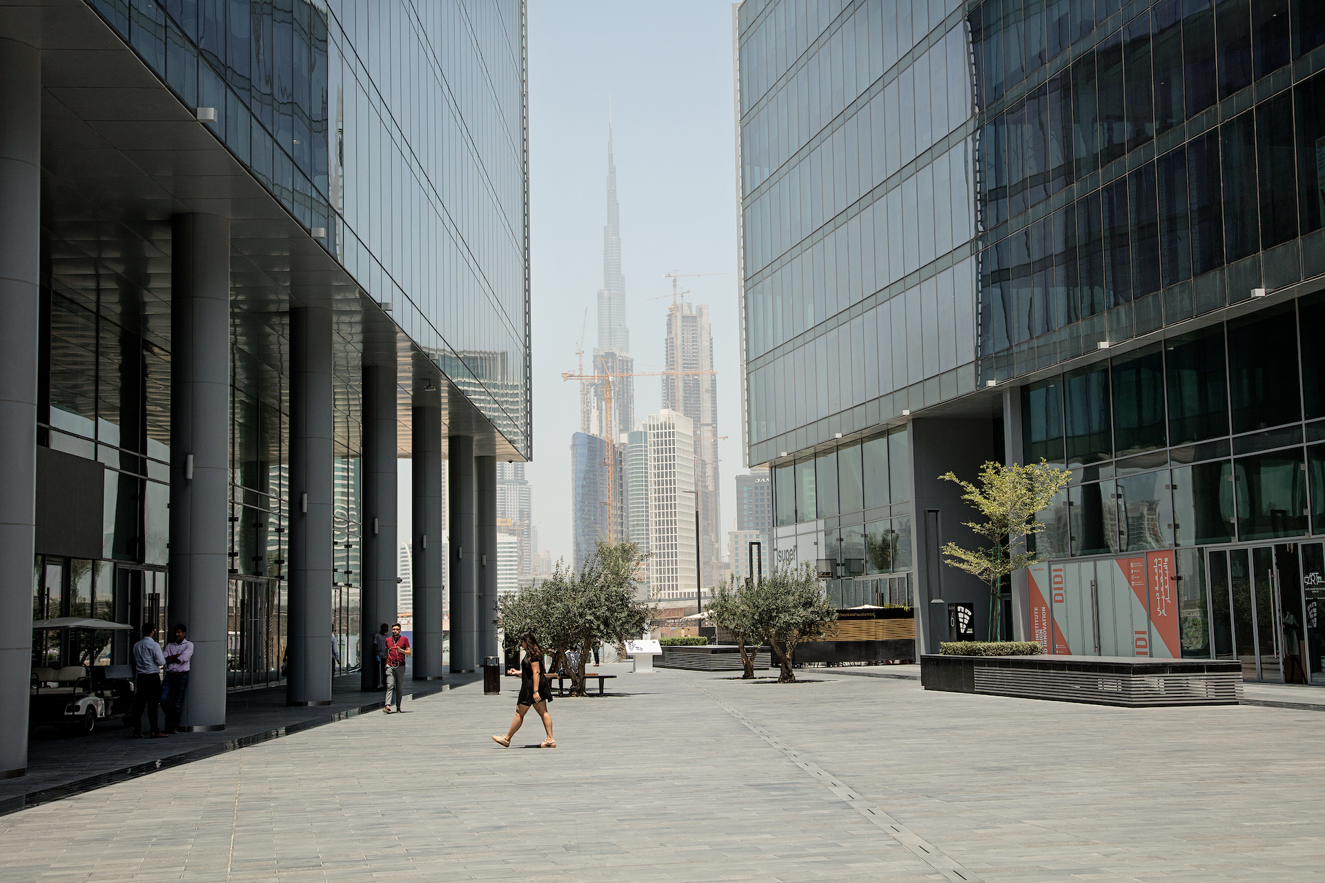 View of Burj Khalifa between two high rise buildings and people walking past
