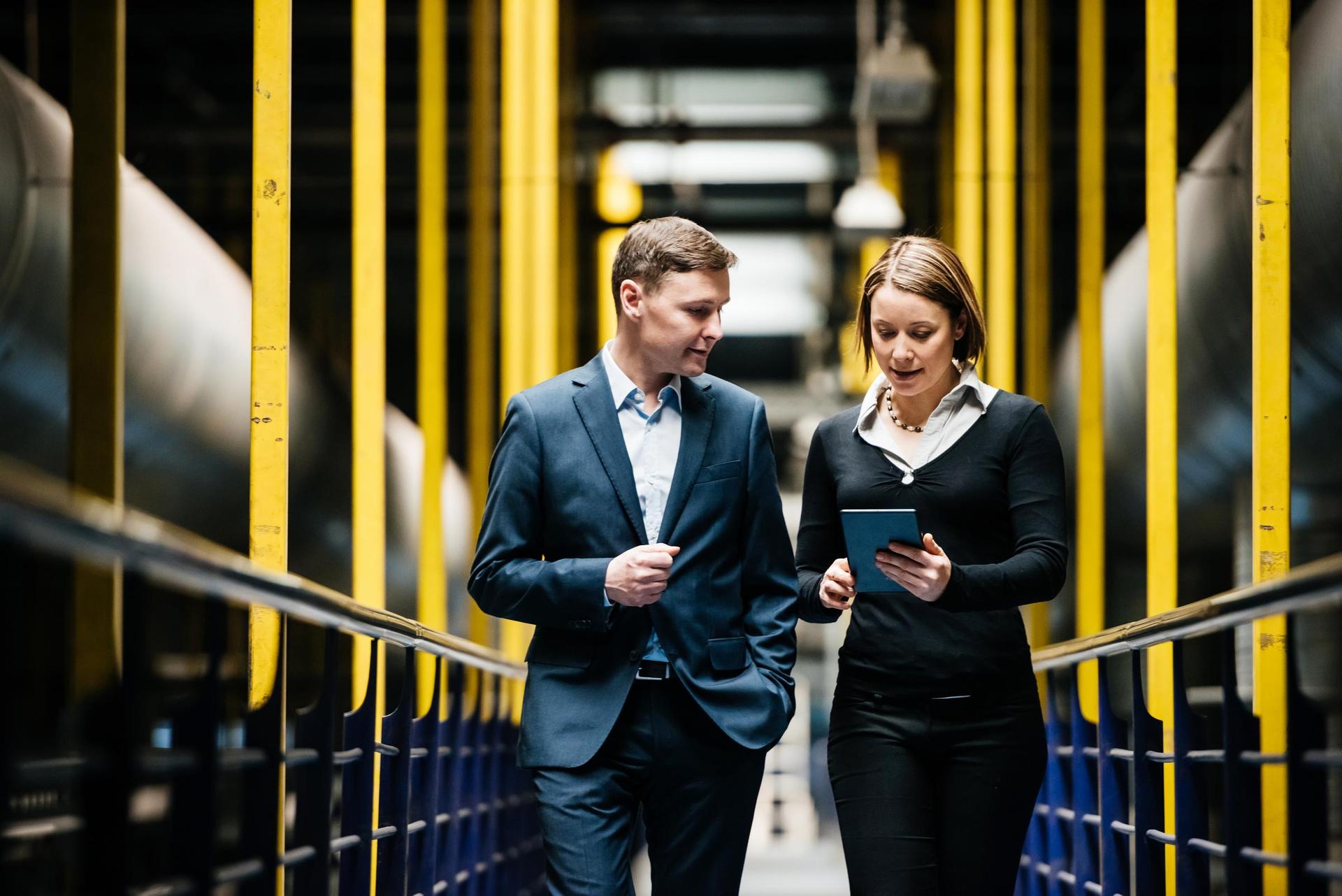 Two Business Person Walking A Dark Factory Hallway and talking about their latest projects