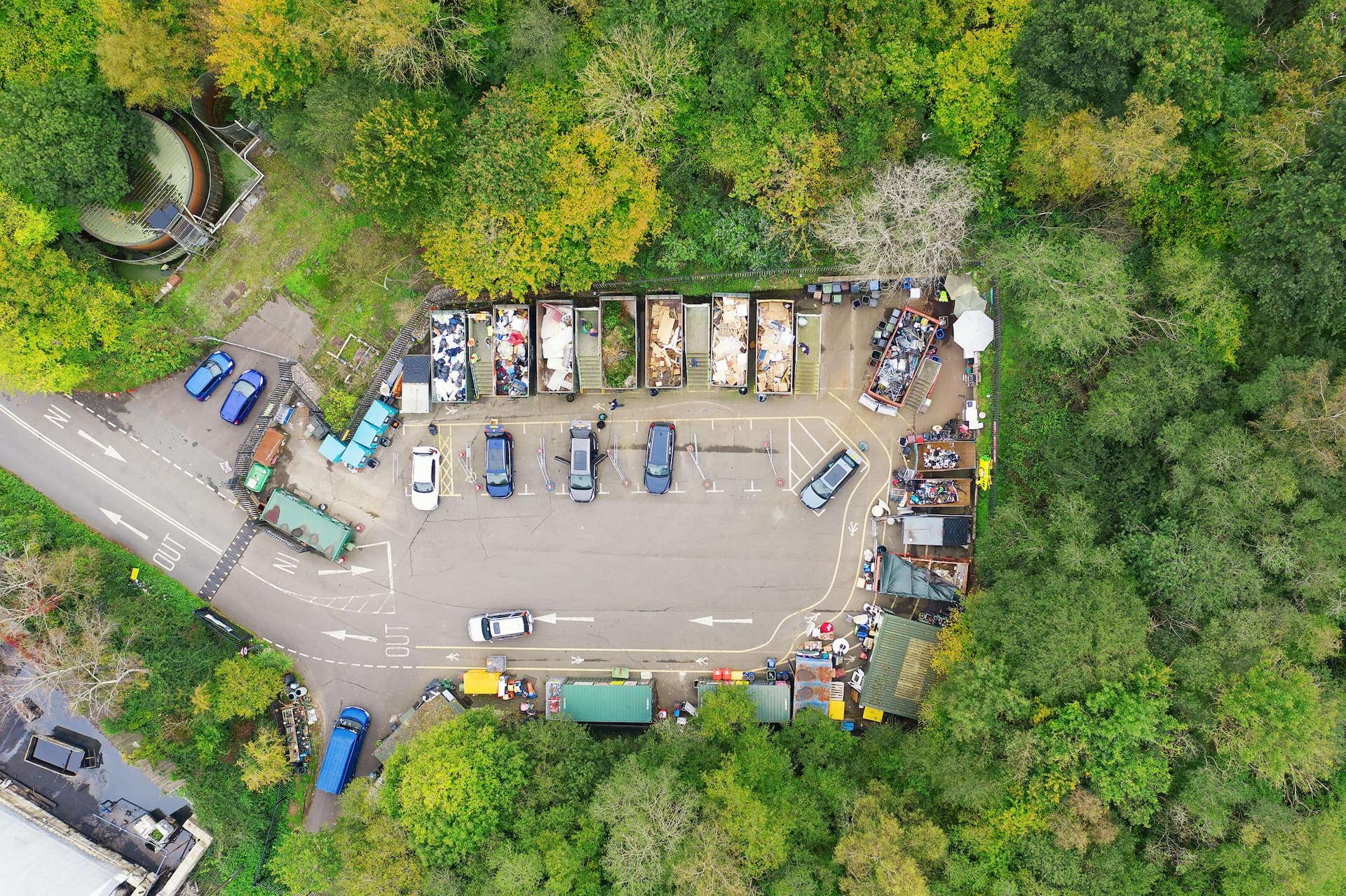 Aerial view of people in cars taking garbage to the waste recycling centre which is surrounded by green trees. Various containers with different rubbish. With Social Distancing.