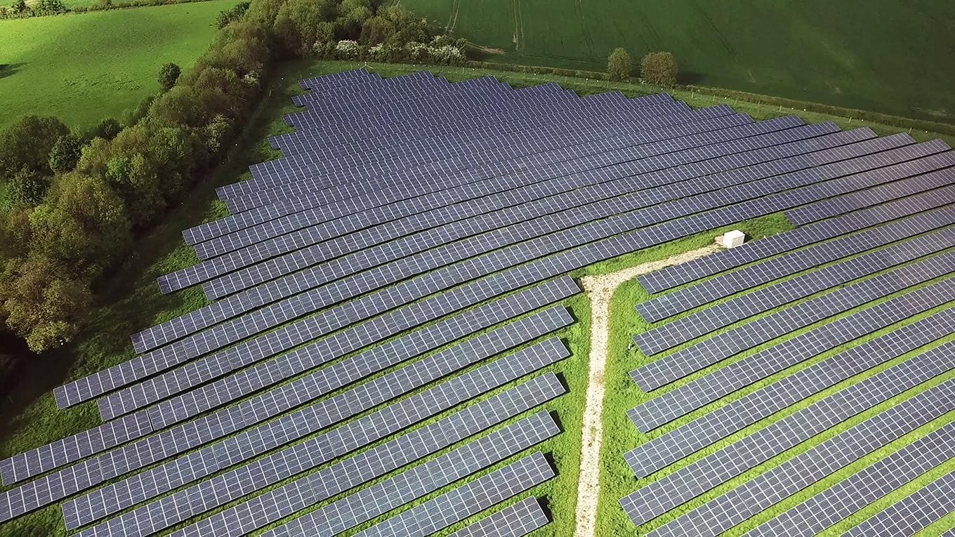 Solar panels farm between agriculture fields in aerial view.